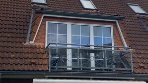 Un edificio residencial con techo de tejas, una ventana central y un balcón con barandilla de metal.