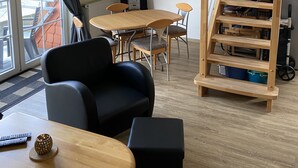 Una sala de estar moderna con una mesa de comedor de madera, sillones negros, una escalera y un ventanal con cortinas.