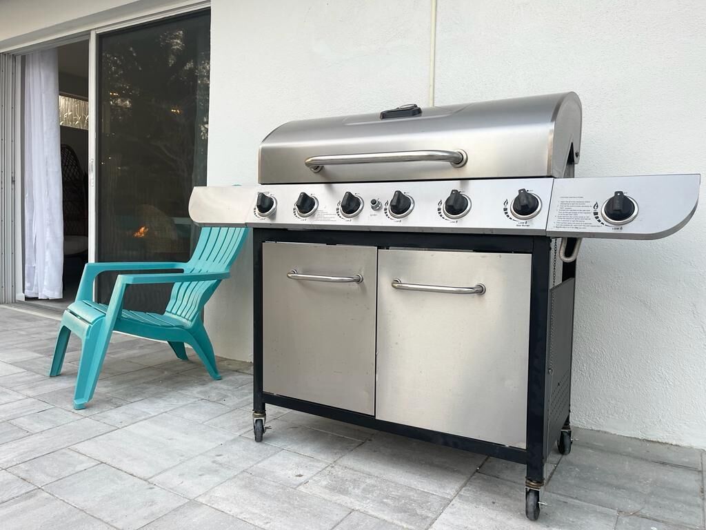 Een draagbare roestvrijstalen grill met vier branders en een extra brander aan de zijkant, gemonteerd op een wielen voorzien trolley.