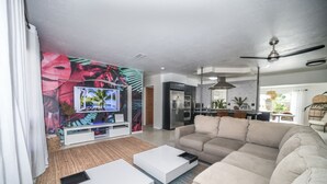Ett modernt vardagsrum med en soffa, två vita soffbord, en platt-TV och ett köksområde i bakgrunden.