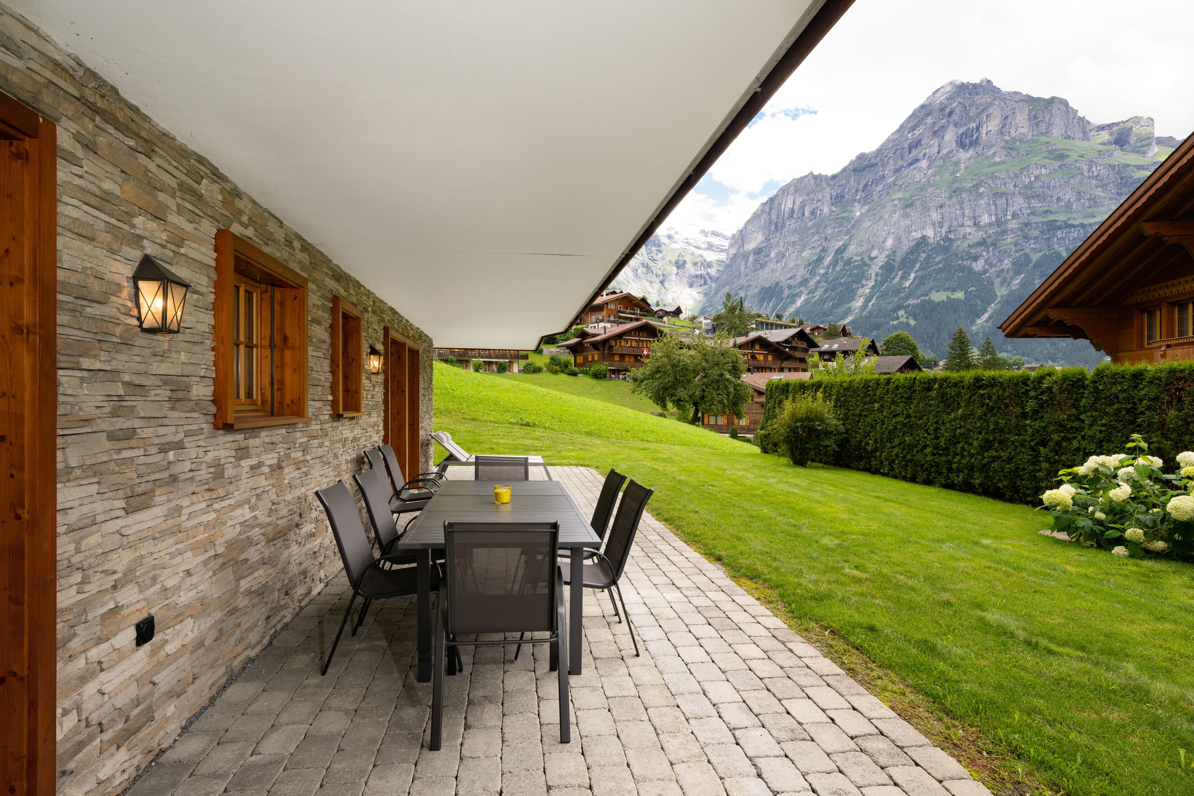 Une terrasse extérieure avec un mur en pierre, des meubles en bois et une vue sur une montagne.