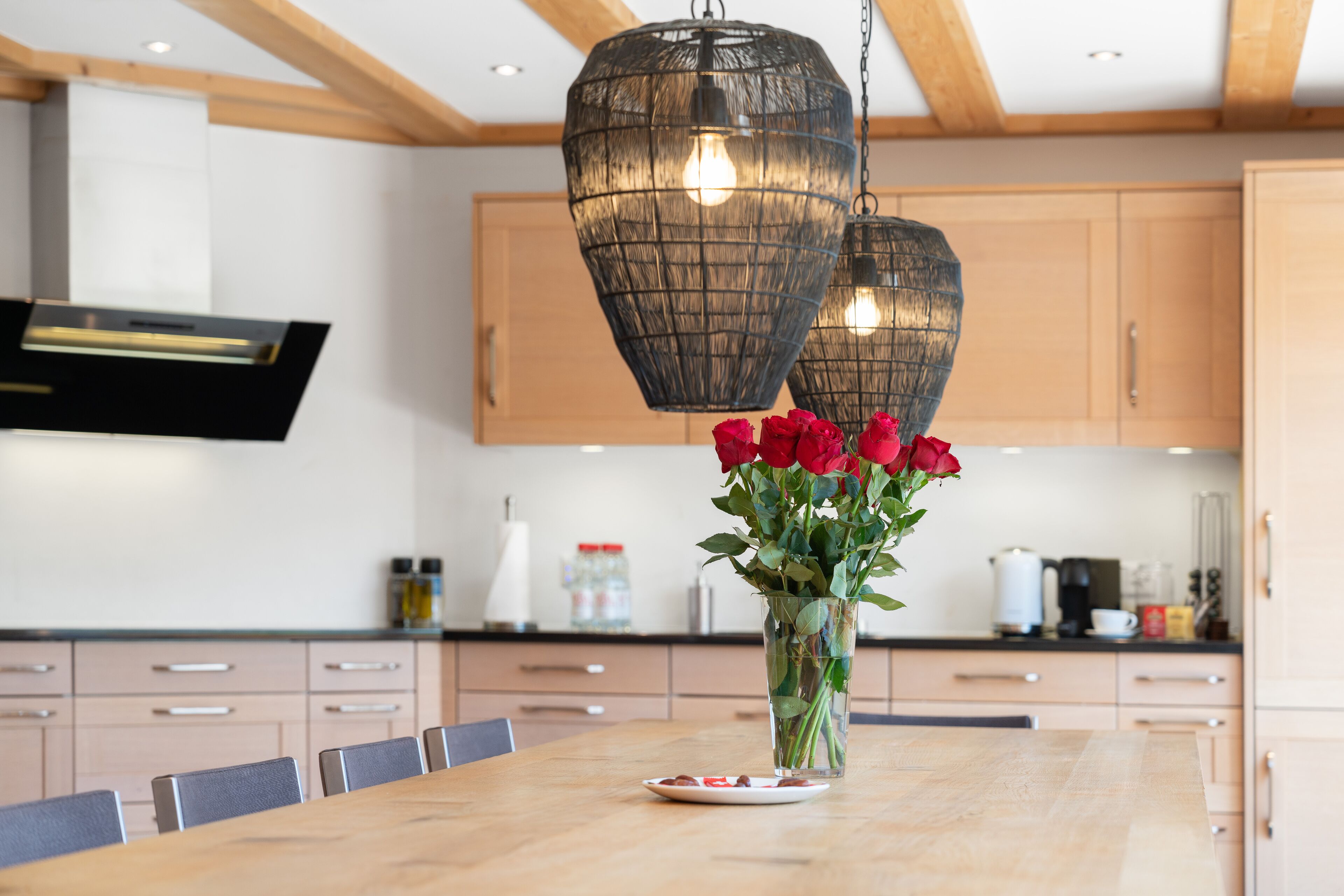 Une cuisine moderne avec des meubles en bois, un îlot central agrémenté d’un vase de roses rouges et des luminaires suspendus.