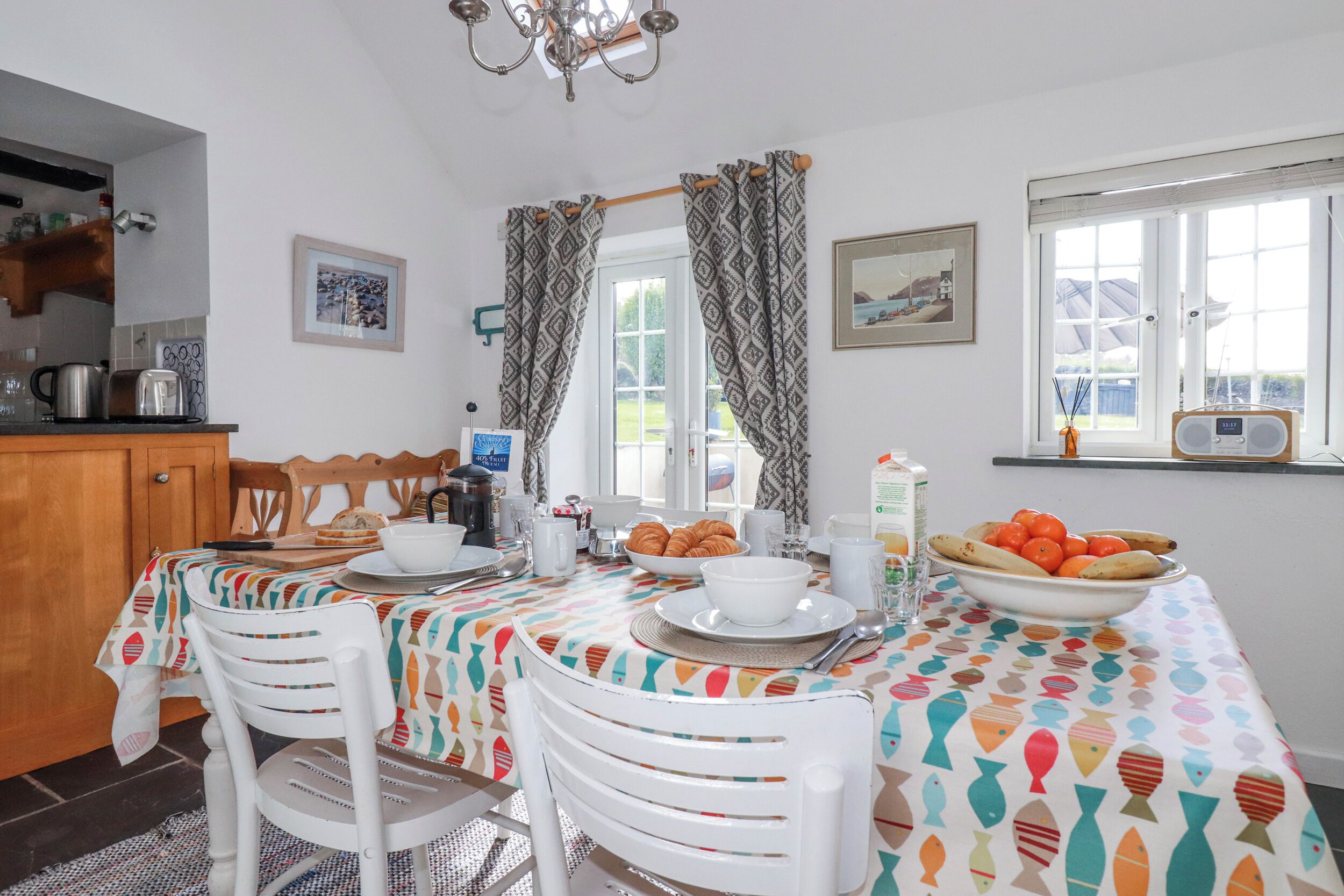 A dining area with a table set for breakfast, chairs, a radio, and a window with curtains.
