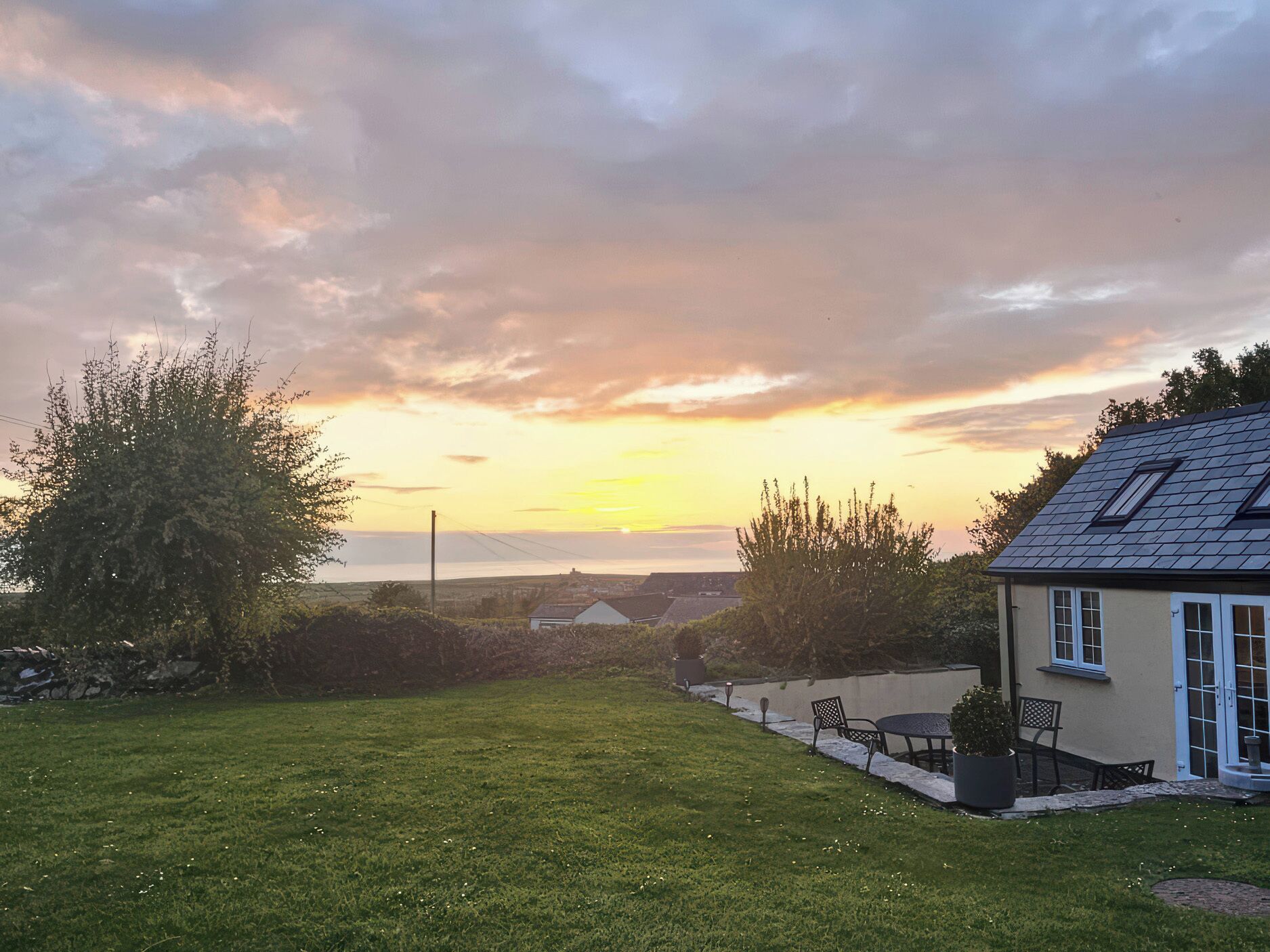 A house with a sloped roof, a lawn, and a view of the sea at sunset.