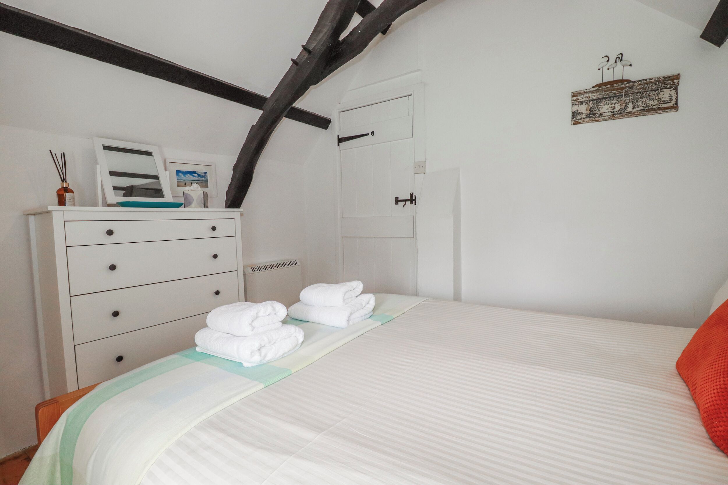 A bedroom with a bed, a dresser, a door, and a wall-mounted artwork.