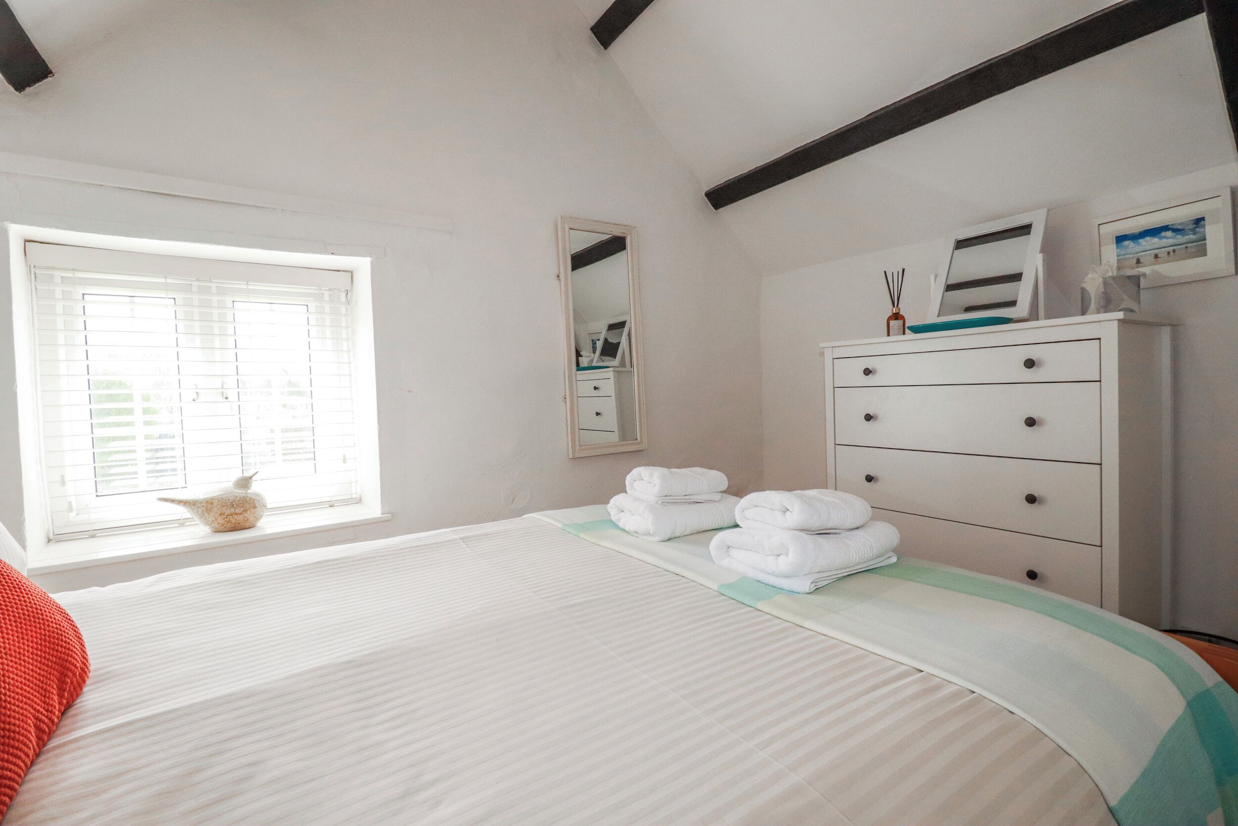 A bedroom with a bed, a dresser, a window, and a mirror.