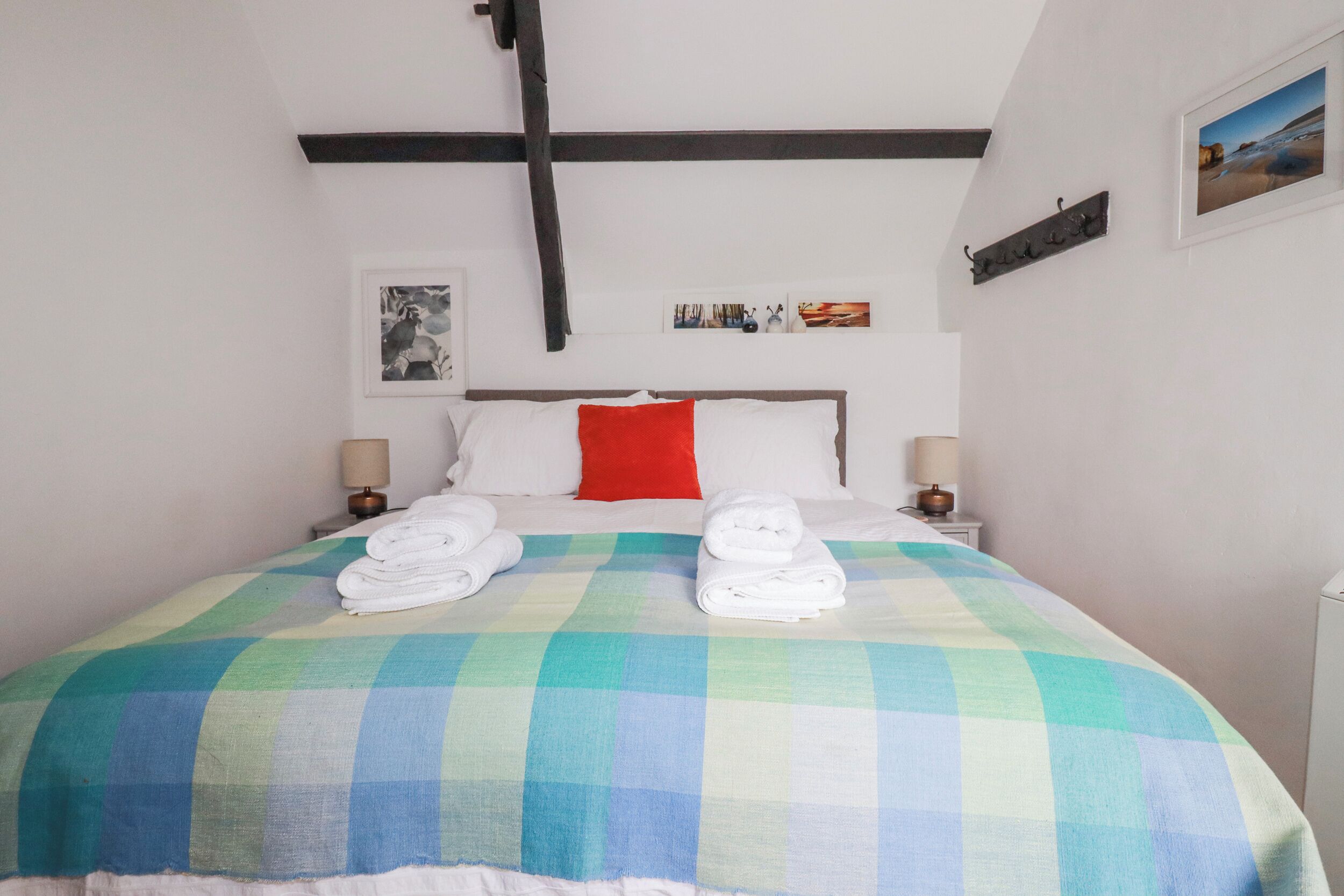 Una habitación de hotel con una cama, dos mesitas de noche con lámparas, una colcha a cuadros y una almohada roja.