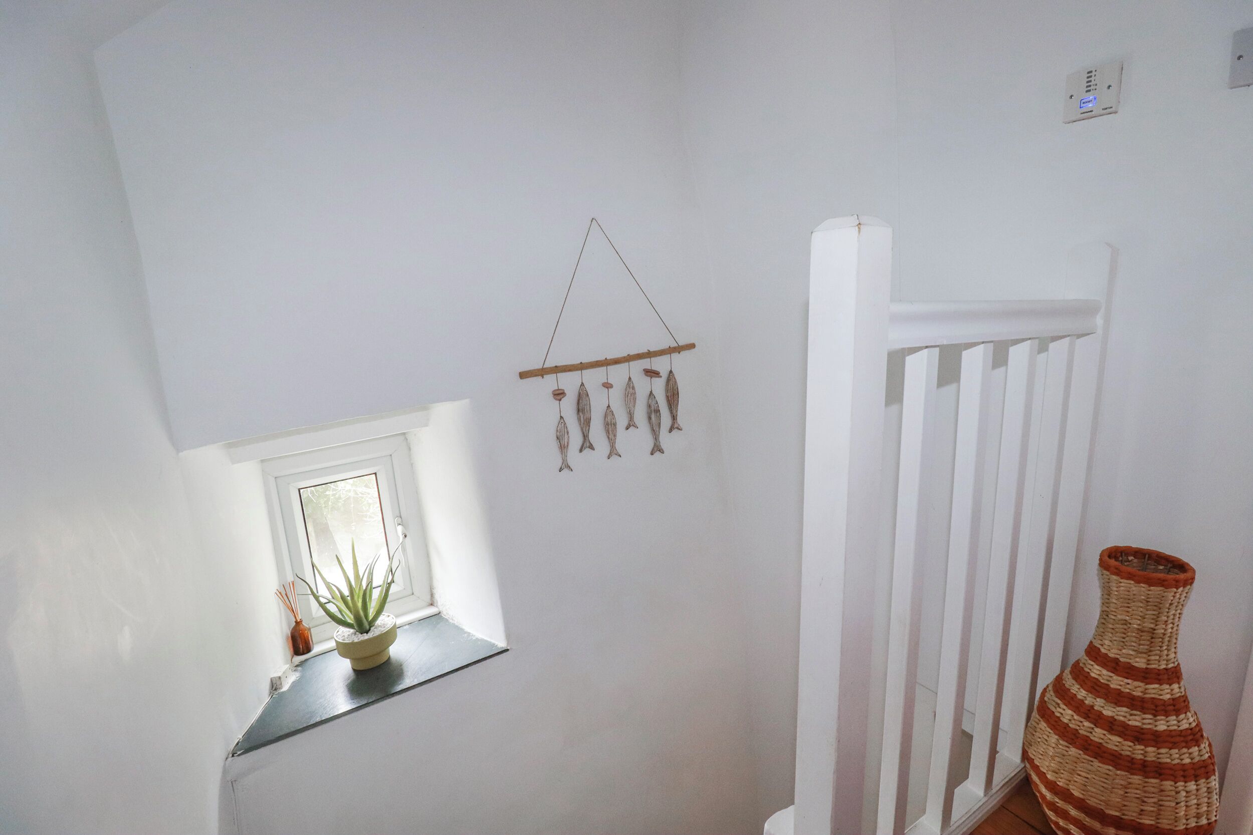 A white interior with a window, a wall-mounted decoration, a white railing, and a woven vase.