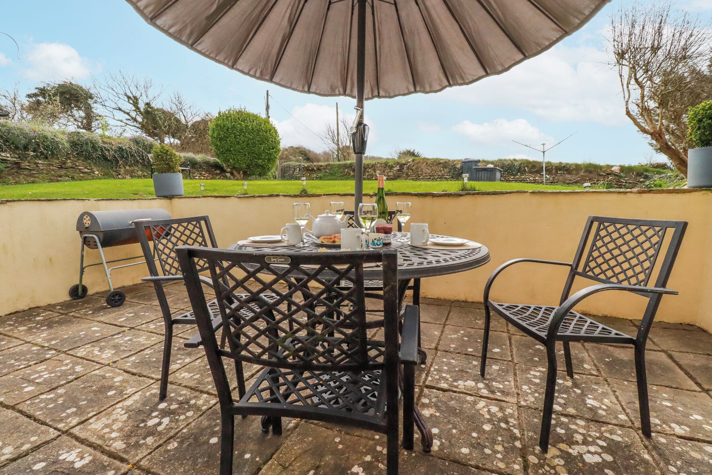 An outdoor patio with a round table, two chairs, a grill, and a large umbrella.