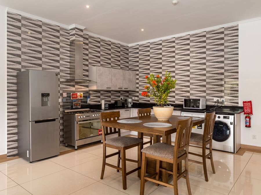 Cocina moderna con refrigerador, horno, microondas y lavadora. Cuenta con una mesa de comedor con sillas y una planta en maceta.