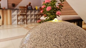 Un espace d’accueil agrémenté d’une pièce maîtresse en pierre, d’un comptoir de réception en bois et d’une plante aux fleurs roses.