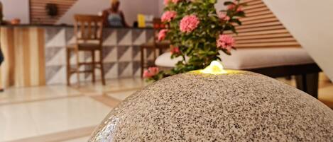 A reception area with a stone centerpiece, wooden reception desk, and a plant with pink flowers.