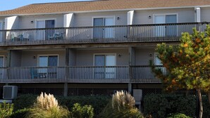 A multi-story building with balconies, air conditioning units, and a pine tree in the foreground. - Catchin' A Dream - 3BR Turtle Cove Unit - Sunset Views, Comm. Pool & Beach (Surf City)