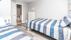 A bedroom with two beds, a white dresser, a bathroom with a shower curtain, and a ceiling fan. - Catchin' A Dream - 3BR Turtle Cove Unit - Sunset Views, Comm. Pool & Beach (Surf City)
