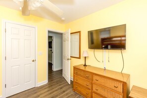 A room with a wooden dresser, a television mounted on the wall, and a door leading to another room.