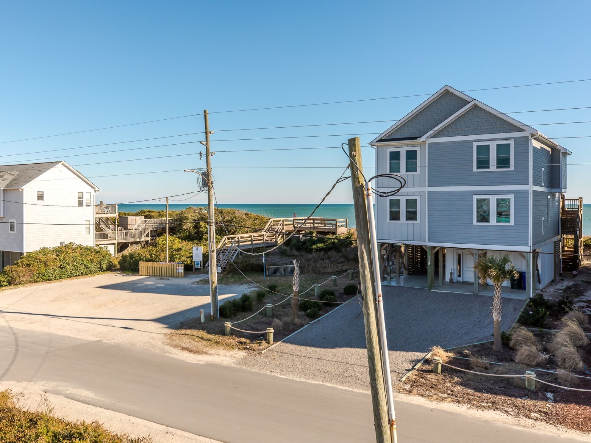A coastal property with a two-story house, a paved driveway, and a wooden bridge leading to a beach.