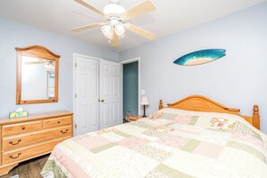 A bedroom with a wooden bed, a dresser, a ceiling fan, a door, and a wall-mounted fish decoration. - No Regrets - 4 BR home in the heart of Surf City!  Dog Friendly! (Surf City)