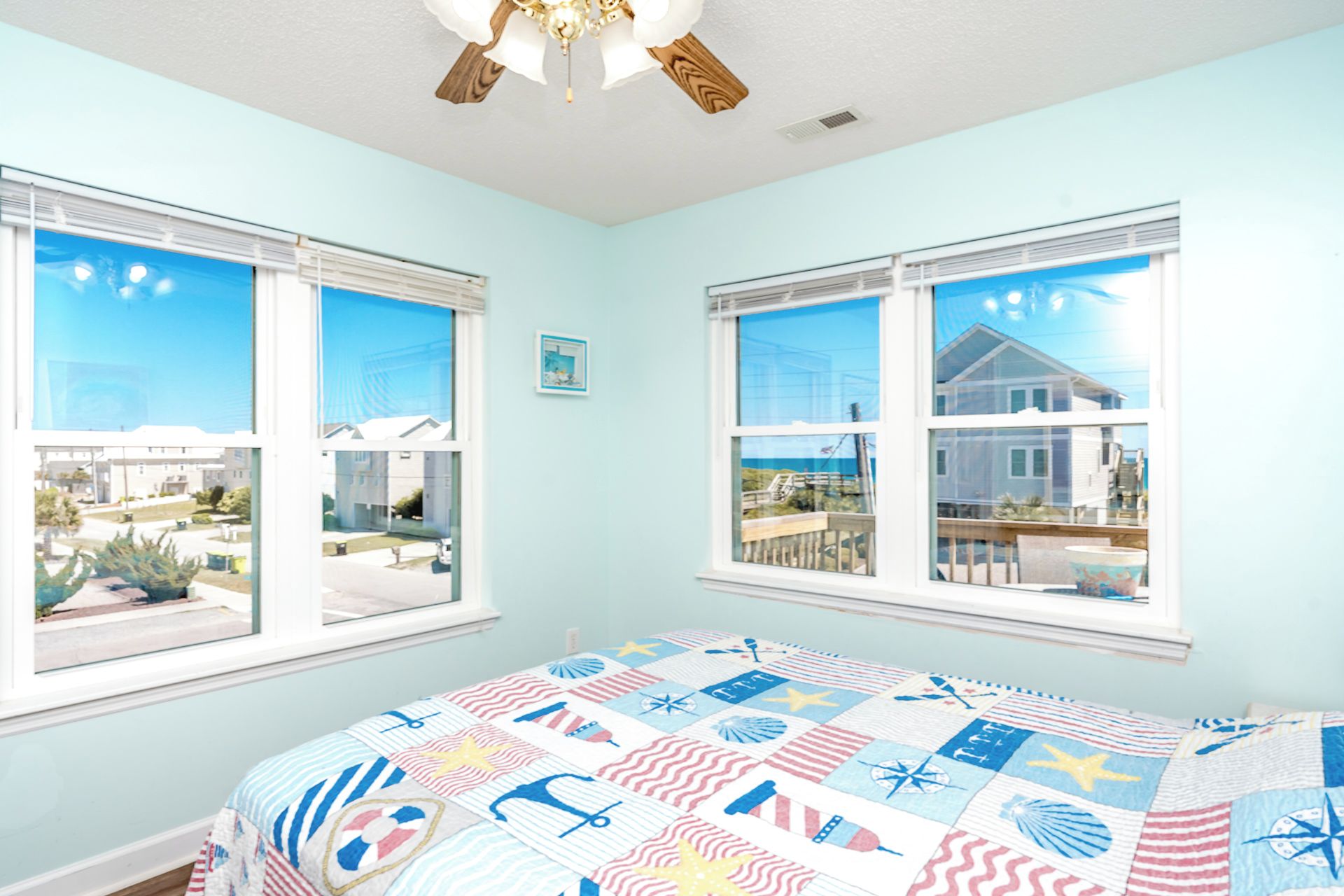 Ein Schlafzimmer mit einem Bett, zwei Fenstern, einem Deckenventilator und Blick ins Freie.