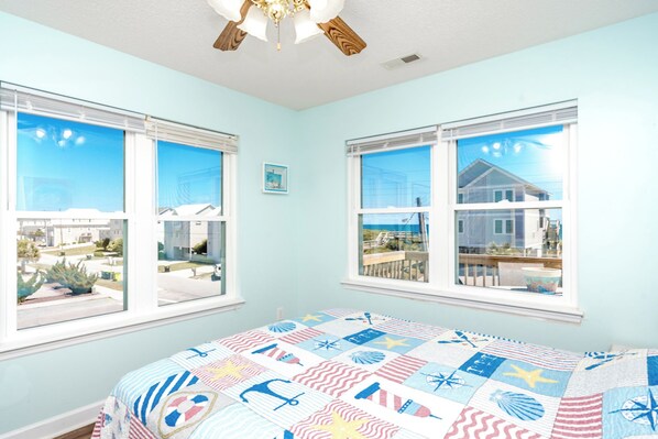 A bedroom with a bed, two windows, a ceiling fan, and a view of the outside. - No Regrets - 4 BR home in the heart of Surf City! Dog Friendly! (Surf City)