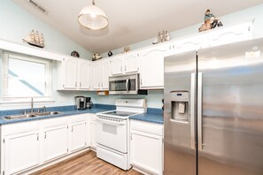 A kitchen with white cabinets, a stainless steel refrigerator, a microwave, a coffee maker, and a water dispenser.