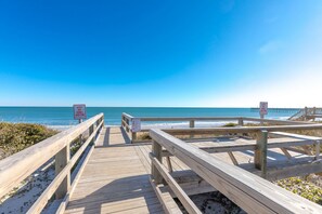 A wooden boardwalk leading to a beach with clear skies.