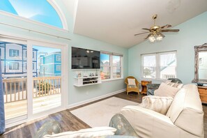 A living room with a large window, a ceiling fan, a television, and a sofa. - No Regrets - 4 BR home in the heart of Surf City!  Dog Friendly! (Surf City)