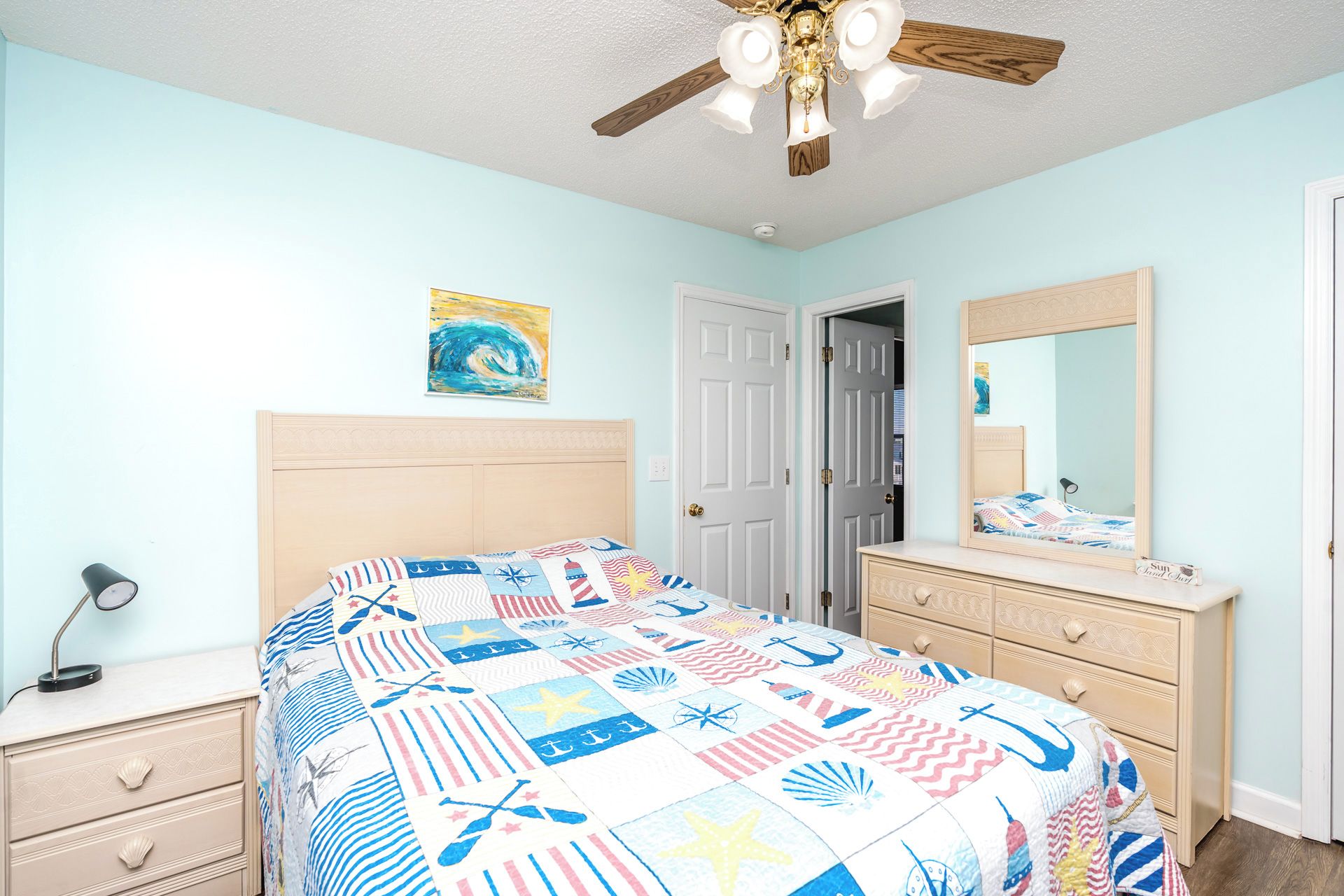 A bedroom with a bed, dresser, nightstand, ceiling fan, and a door.