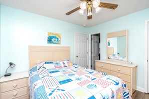 A bedroom with a bed, dresser, nightstand, ceiling fan, and a door.