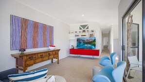 A modern living room with a wooden cabinet, a red entertainment unit, a large TV, and blue chairs. - Ocean View Villa Marco (Marcus Beach)