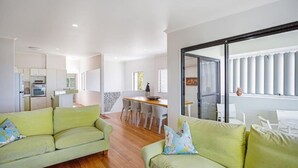 A modern living room with a green sofa set, a dining area with a wooden table, and a kitchen with white cabinets and appliances. - Ocean View Villa Marco (Marcus Beach)