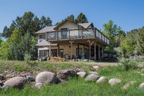 Una casa de dos pisos con un balcón, rodeada de árboles y rocas.