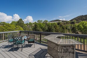 Una terraza de madera con mobiliario exterior, incluyendo sillas y una mesa, con vistas a una ladera boscosa.