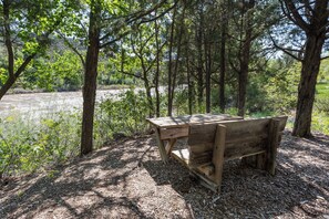 A wooden bench in a wooded area with a river in the background.