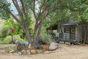 A rustic cabin with a porch, surrounded by trees and rocks.
