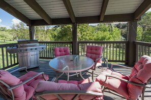 A covered outdoor patio with a grill, round glass table, and pink cushioned chairs.
