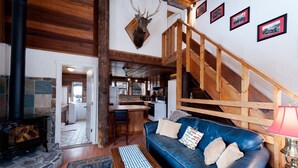 A cozy cabin interior with a stone fireplace, a blue leather sofa, a wooden staircase, and framed pictures on the wall. - Pet Friendly Rustic Cabin on the Animas River -  6 Min. to Downtown Durango (Durango)
