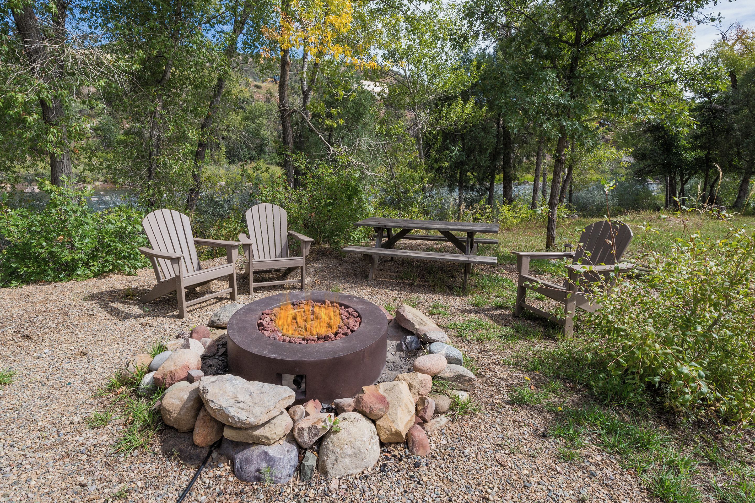 A fire pit surrounded by rocks and wooden chairs in a natural setting.