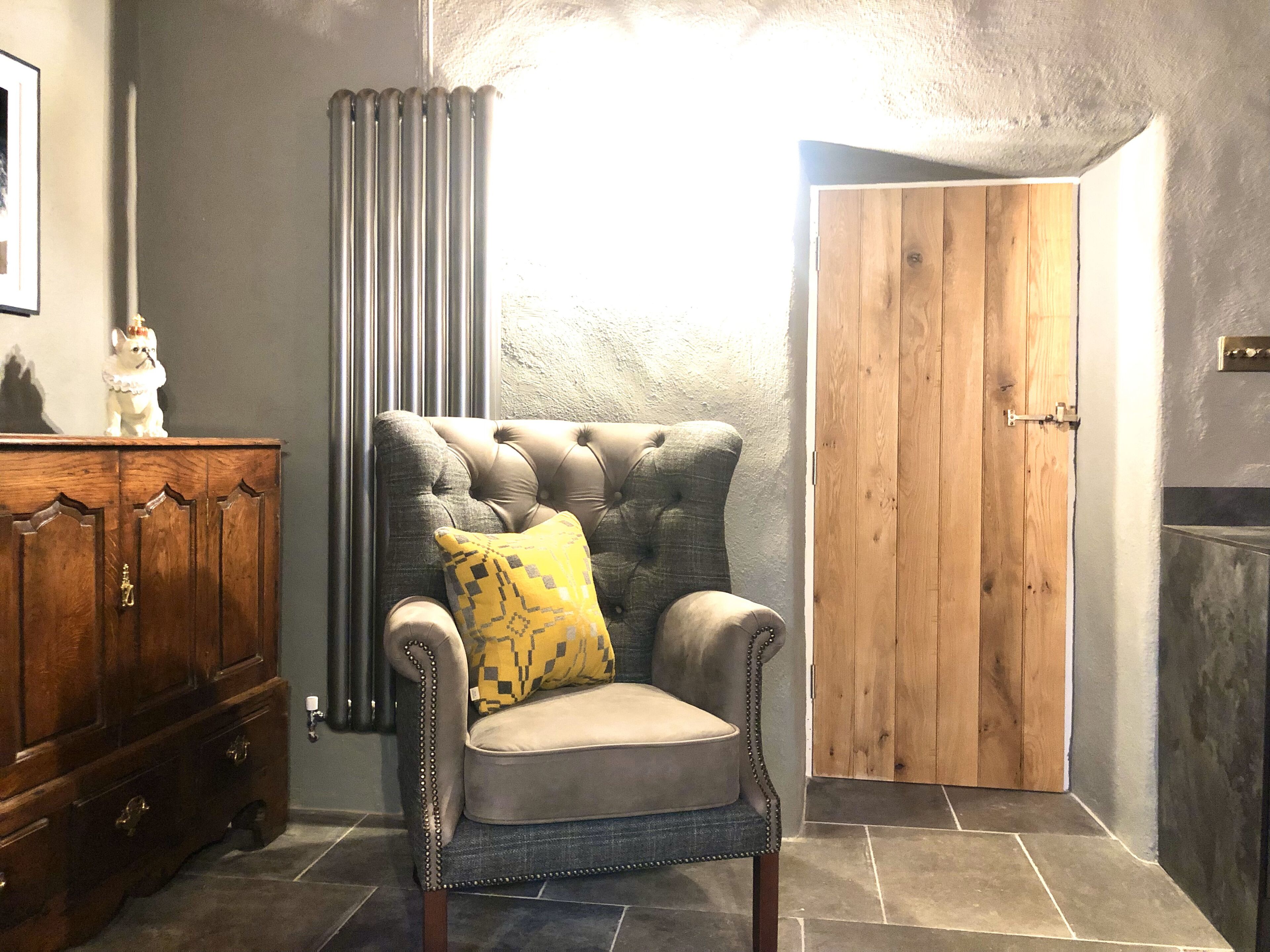 A room with a tufted armchair, a wooden cabinet, a radiator, and a wooden door.