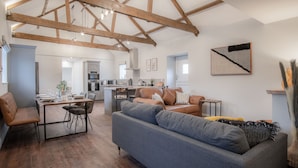 Un vaste espace de vie doté d’un haut plafond et de poutres apparentes, une table à manger avec des chaises, un canapé et une cuisine à l’arrière-plan.