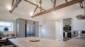 Une cuisine moderne dotée d’un grand îlot central, d’appareils électroménagers intégrés et de poutres apparentes en bois.
