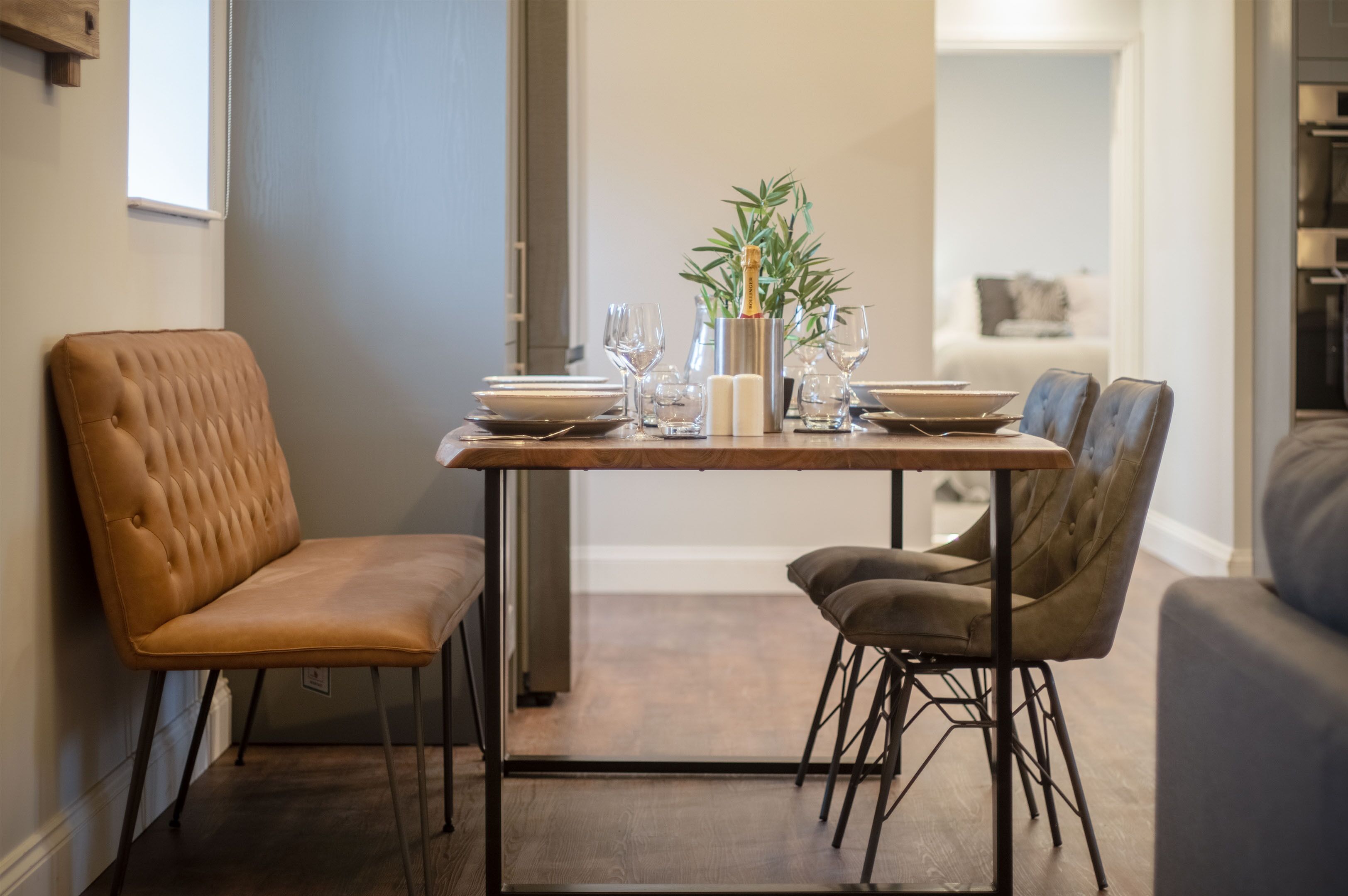 Comedor con mesa de madera, dos sillas, una planta en maceta y una botella de champán.