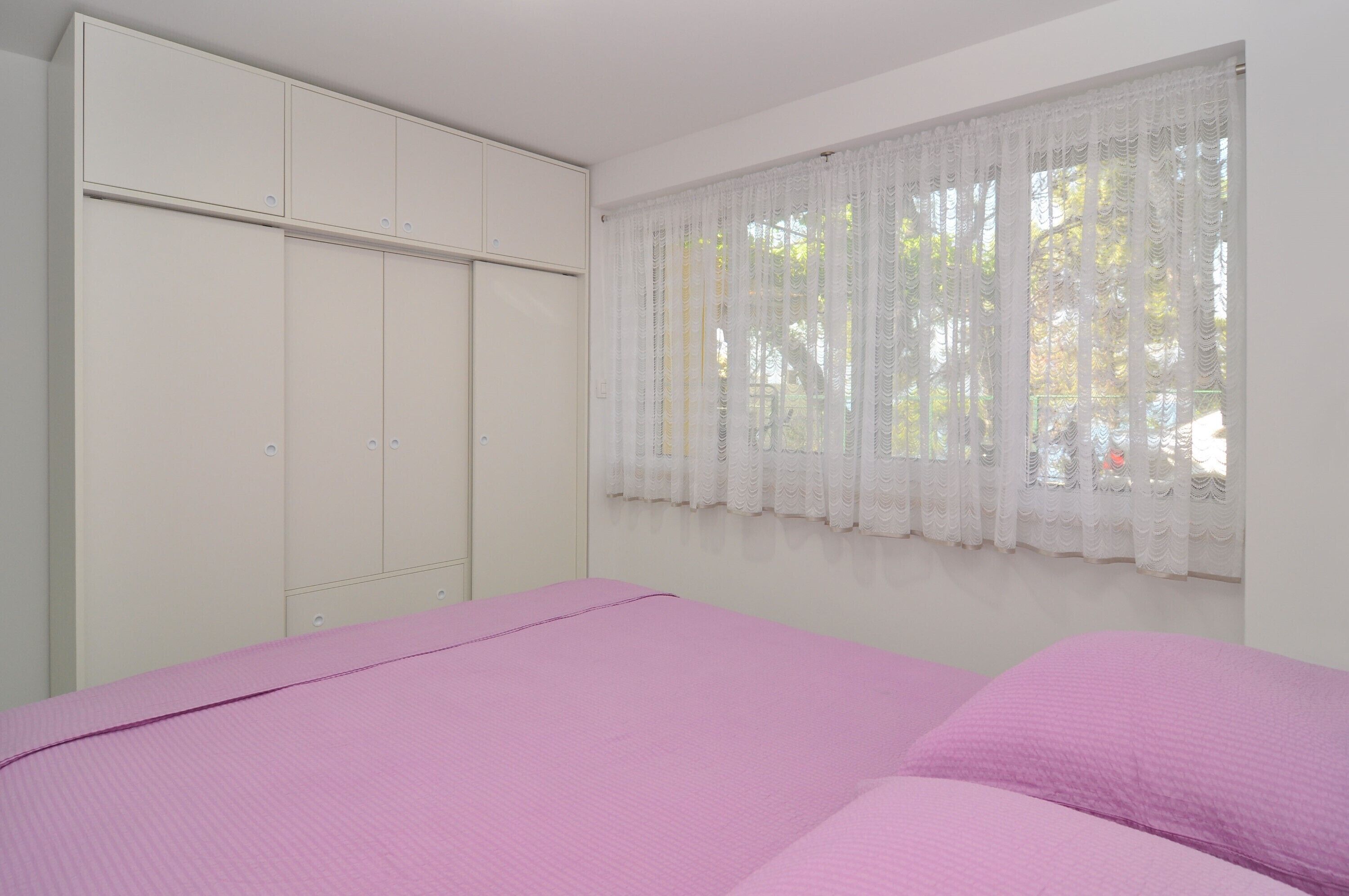 Un dormitorio con cama, armario y ventana con cortinas de gasa.