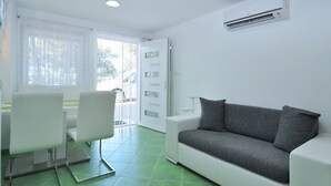 Un saló modern amb un sofà blanc, una taula de dinar amb cadires i un gran finestral amb cortines translúcides.