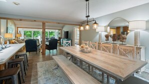 A spacious kitchen with a long wooden table, a dining area, and a view of the outdoors.