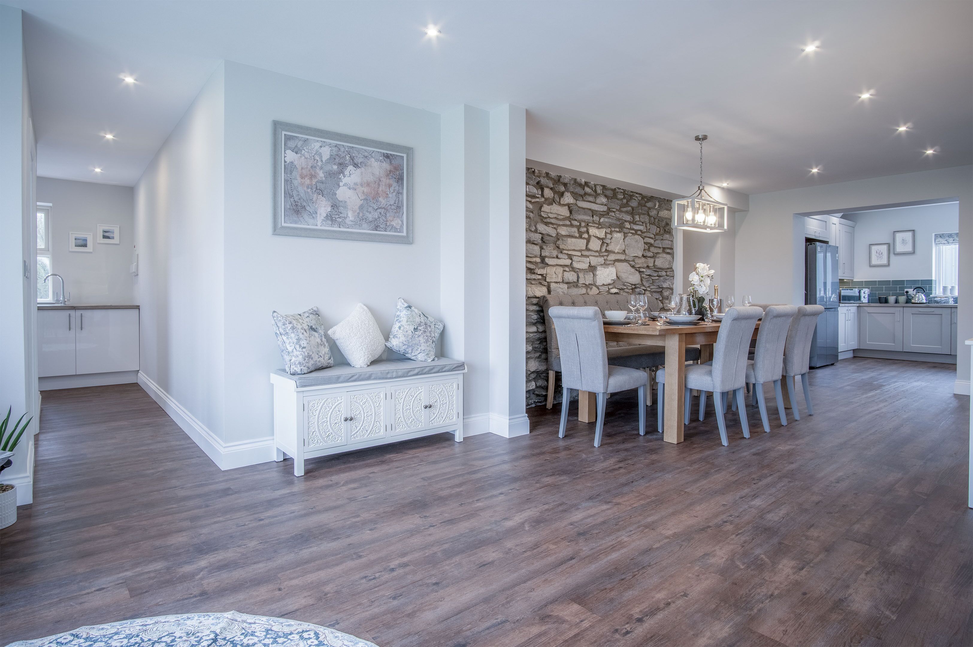 A modern kitchen with a stone accent wall, a dining area with a wooden table and chairs, and a built-in bench with decorative pillows.