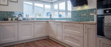 A kitchen with white cabinets, a window with a floral valance, a stainless steel range hood, and a tiled backsplash.