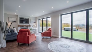A spacious living room with a fireplace, large windows, and a view of the outdoors. - Kiln Park Farmhouse - 4 Bedroom Cottage - Narberth (Narberth)