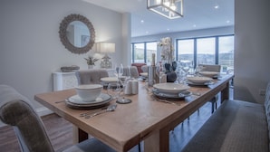 A dining area with a long wooden table set for four, a large mirror, and a view of the city through large windows. - Kiln Park Farmhouse - 4 Bedroom Cottage - Narberth (Narberth)