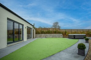 Een modern gebouw met grote glazen deuren, een kunstgrasveld en een betonnen pad.