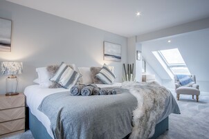 Un dormitorio moderno con una cama grande, una mesita de noche, una lámpara y vistas del cielo a través de un tragaluz.